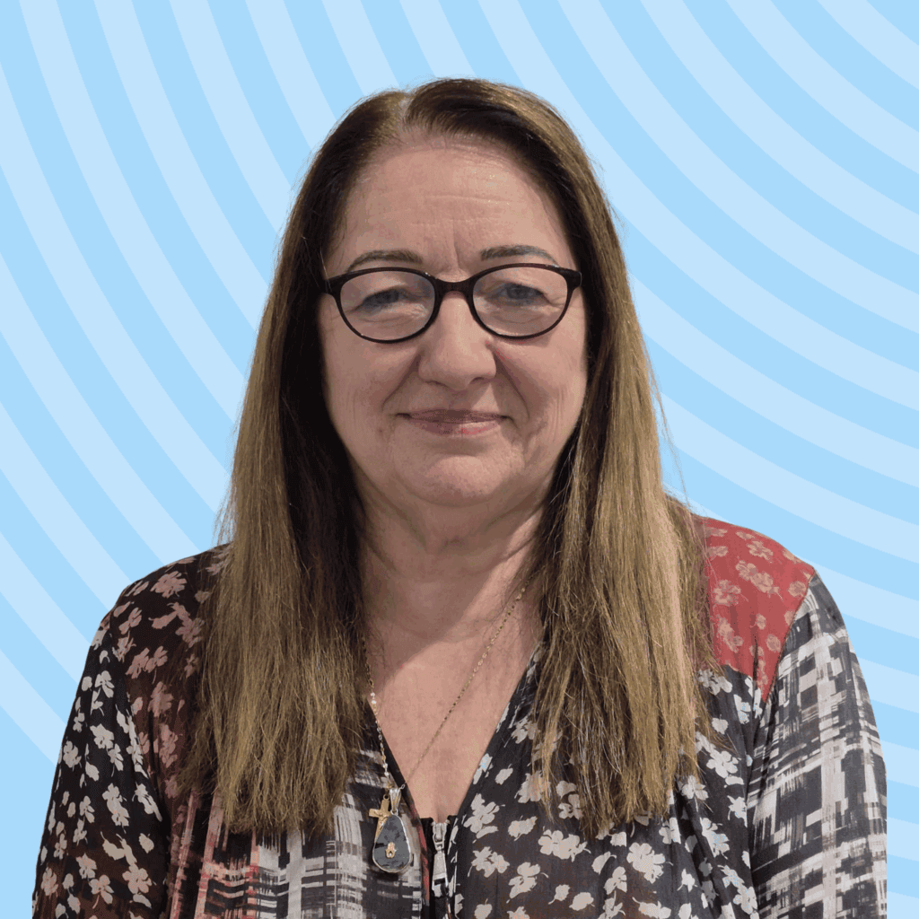 Agnes, a white woman wearing glasses and a plain top, posed against a blue background.