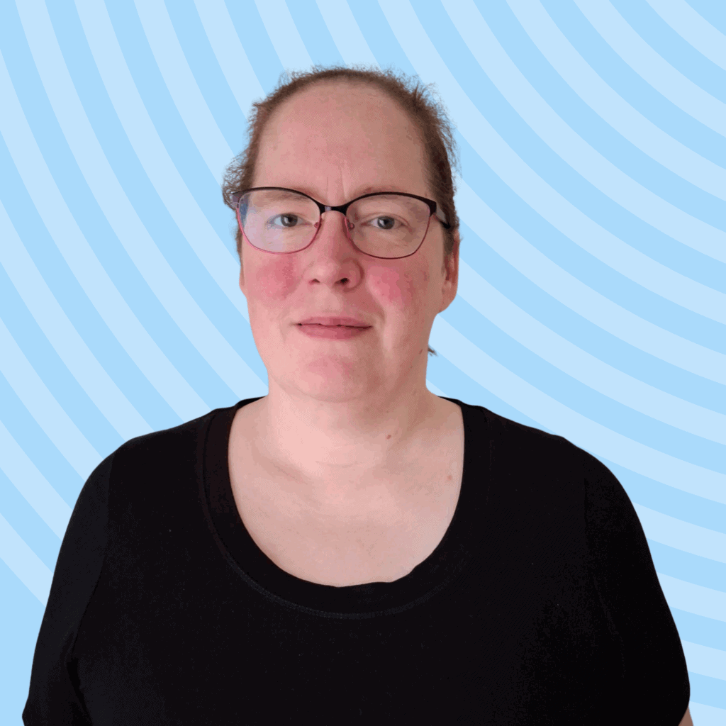 Angela, a white woman wearing a black t-shirt and glasses, posed against a blue background.